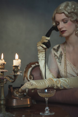 Retro 1920s fashion woman on the phone while sitting on sofa beside table with candlestick and...