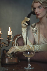 Retro 1920s fashion woman on the phone while sitting on sofa beside table with candlestick and...