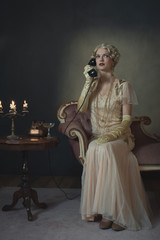 Retro 1920s fashion woman on the phone while sitting on sofa beside table with candlestick and...