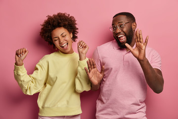 Indoor shot of glad girlfriend and boyfriend dance hip hop with joy, celebrate something, laugh and...
