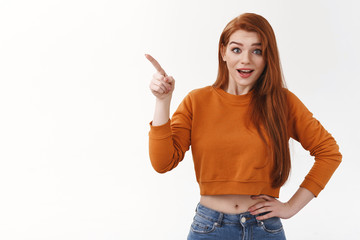 Surprised happy impressed redhead ginger girl wear makeup stylish cropped top pointing upper left corner index finger indicate awesome gift look camera astonished pleased smiling joyfully