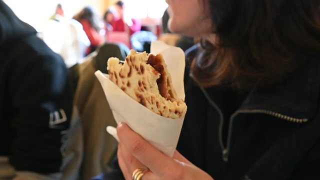 Ravenna, Italy, December 2019. An indistinguishable Caucasian woman is eating a Romagna piadina, an Italian specialty highly appreciated by tourists. You can see the tasty filling of ham and cheese.