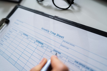 Person's Hand Filling Blank Weekly Time Sheet