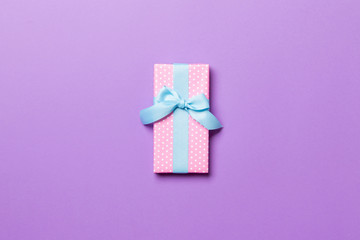 Gift box with blue bow for Christmas or New Year day on purple background, top view with copy space