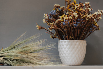 Dried wildflowers. Many tiny blue and yellow flowers in a white vase. Bouquet on a gray background.