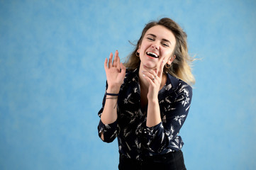 Concept woman in a dark blouse smiling talking. Portrait of a model girl with excellent makeup with curly hair and good teeth in the studio on a blue background.