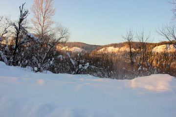 snow-covered hills, evergreen trees on the slopes, in the sunset. Lots of snow and frost trees. 