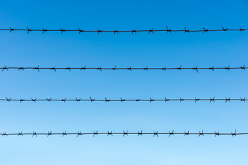 four rows of barbed wire against a blue sky