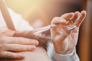 Close up of male hairdresser cutting hair with scissors, brown tinting, barber shop concept