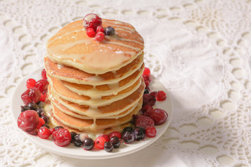 Homemade pancakes with berries and  condensed milk on white plate isolated