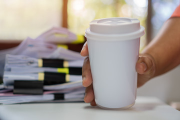 Paper coffee cup mock-up. Businessman holding white cardboard cup for logo with document paperwork on meeting. Concept of business people working in office and save world. Mockup for word