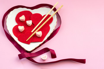 Felt hearts with chopstick and marshmallows on the heart-shaped plate on pink background. Valentine's Day concept.