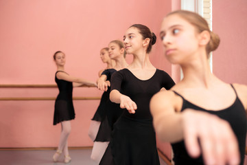 Small group of beautiful teenage girls in black dresses practicing classical ballet moves in a traditional ballet studio