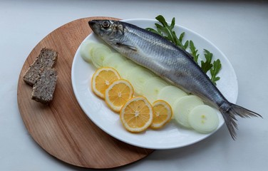 Salted fish - herring with onions, buckwheat bread and herbs, on a wooden board and white background. With crumpled craft paper. Yummy.