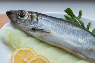 Salted fish - herring with onions, buckwheat bread and herbs, on a wooden board and white background. With crumpled craft paper. Yummy.