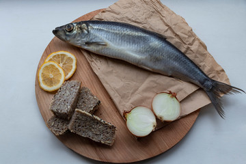 Salted fish - herring with onions, buckwheat bread and herbs, on a wooden board and white background. With crumpled craft paper. Yummy.