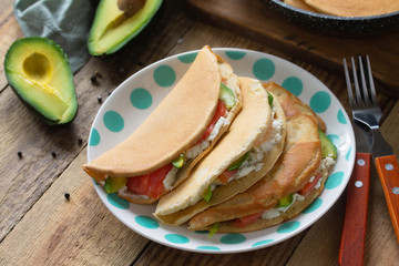 The concept of a healthy breakfast or snack. Oat pancakes stuffed with cottage cheese, salmon and avocado in a plate on rustic wooden table. Copy space.