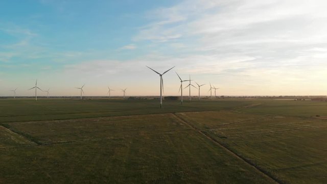Windmill - wind power plant turbines on green fields at sunset during summer, aerial drone shot European Union area.
