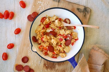 Rice paella with chorizo, tomato and chicken in pan on wooden background