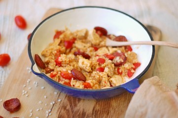 Rice paella with chorizo, tomato and chicken in pan on wooden background