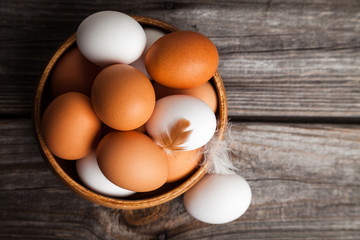 Fresh white and brown chicken eggs in a wooden bowl. Raw eggs on wooden background