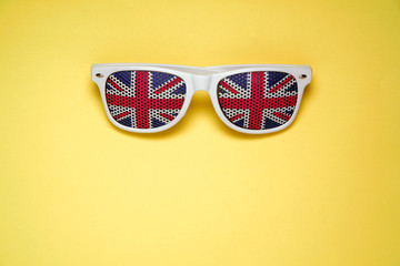 White rimmed sunglasses with UK flag on a yellow isolated background. Free space for text.