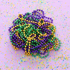 Multi colored mardi gras beads, blue, green, yellow, pink, purple and gold over purple background
