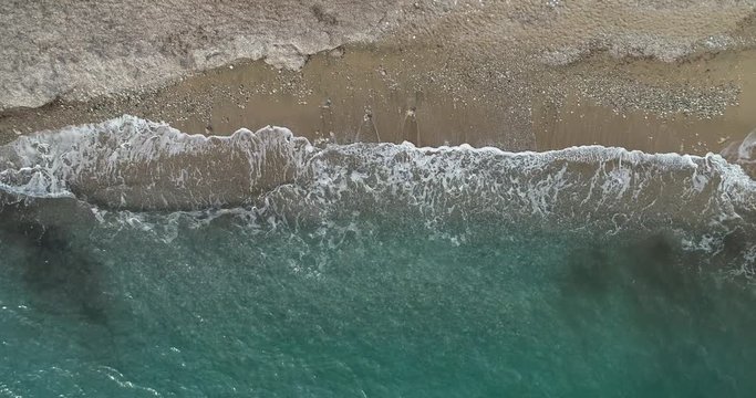 Aerial view of drone flying above beautiful beach with views of ocean waves and water crashing on to sandy beach from top angle