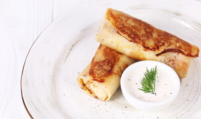 Pancakes with meat and sour cream on a white background