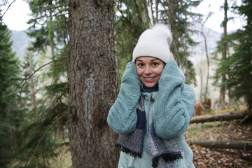 Portrait of a young happy woman in a white knitted hat with a bubo and in seasonal clothes in the winter forest. Winter concept.