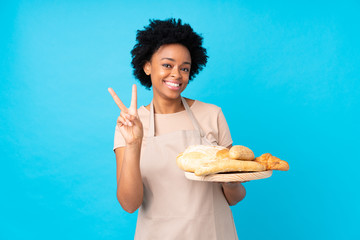 African american woman in chef uniform. Female baker holding a table with several breads smiling...