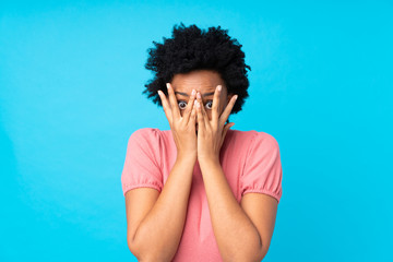 African american woman over isolated blue background covering eyes and looking through fingers