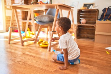 Beautiful african american toddler sitting on the floor and smiling around lots of toys at kindergarten