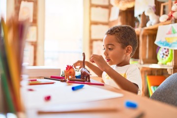 Beautiful african american toddler playing with dinosaurs toy on desk at kindergarten