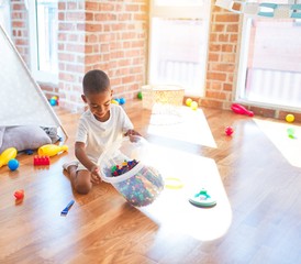 Adorable african american toddler playing with building blocks around lots of toys at kindergarten