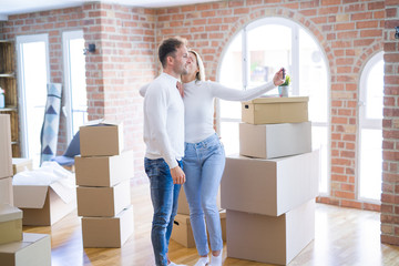 Fototapeta na wymiar Young beautiful couple standing using smartphone to take selfie kissing at new home around cardboard boxes