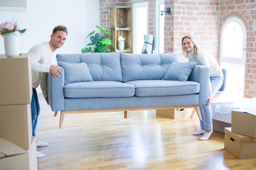 Young beautiful couple moving sofa at new home around cardboard boxes