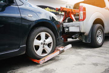 Tow truck picking up and towing old broken down car on a roadside