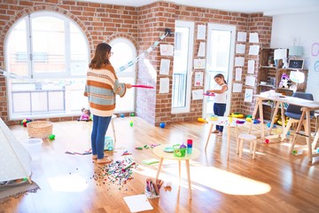 Beautiful teacher and toddler playing tennis using racket around lots of toys at kindergarten