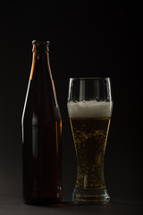 Golden beer in a bottle and in a glass and snack nuts, squid and chips on a black background