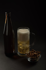 Golden beer in a bottle and in a glass and snack nuts, squid and chips on a black background