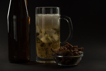 Golden beer in a bottle and in a glass and snack nuts, squid and chips on a black background