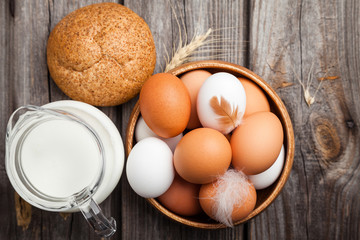 Fresh white and brown chicken eggs in a wooden bowl, milk, bread, and wheat ears. Raw eggs on wooden background