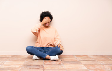 African american woman sitting on the floor covering eyes by hands. Do not want to see something