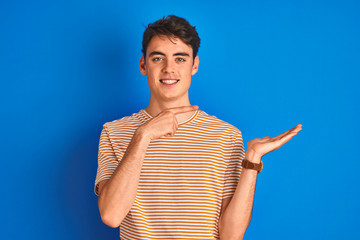 Teenager boy wearing casual t-shirt standing over blue isolated background amazed and smiling to...