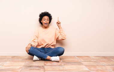 African american woman sitting on the floor intending to realizes the solution while lifting a finger up