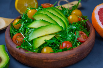 a plate with a fresh salad with arugula, cherry tomatoes and avacado, bright green on a black background, avacado and grapefruit cut in half