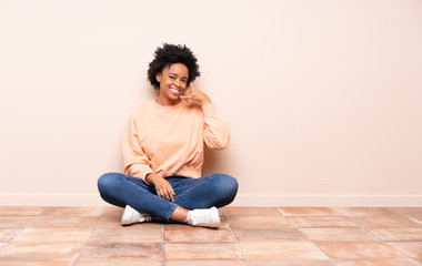 African american woman sitting on the floor making phone gesture. Call me back sign