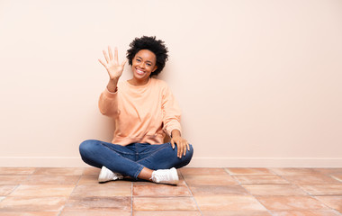 African american woman sitting on the floor counting five with fingers