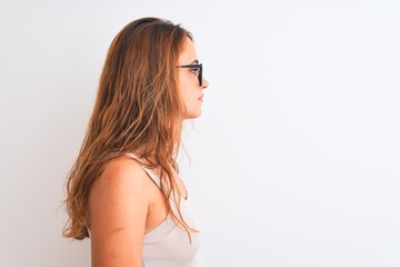 Young redhead woman wearing glasses standing over white isolated background looking to side, relax profile pose with natural face with confident smile.